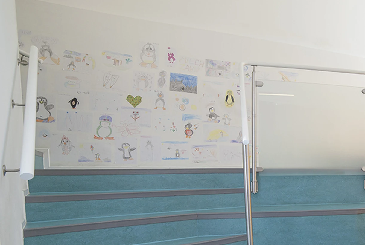 Wand im Treppenhaus der Praxis Gerlingen, über und über behängt mit von Kindern gemalten Pinguin-Bildern